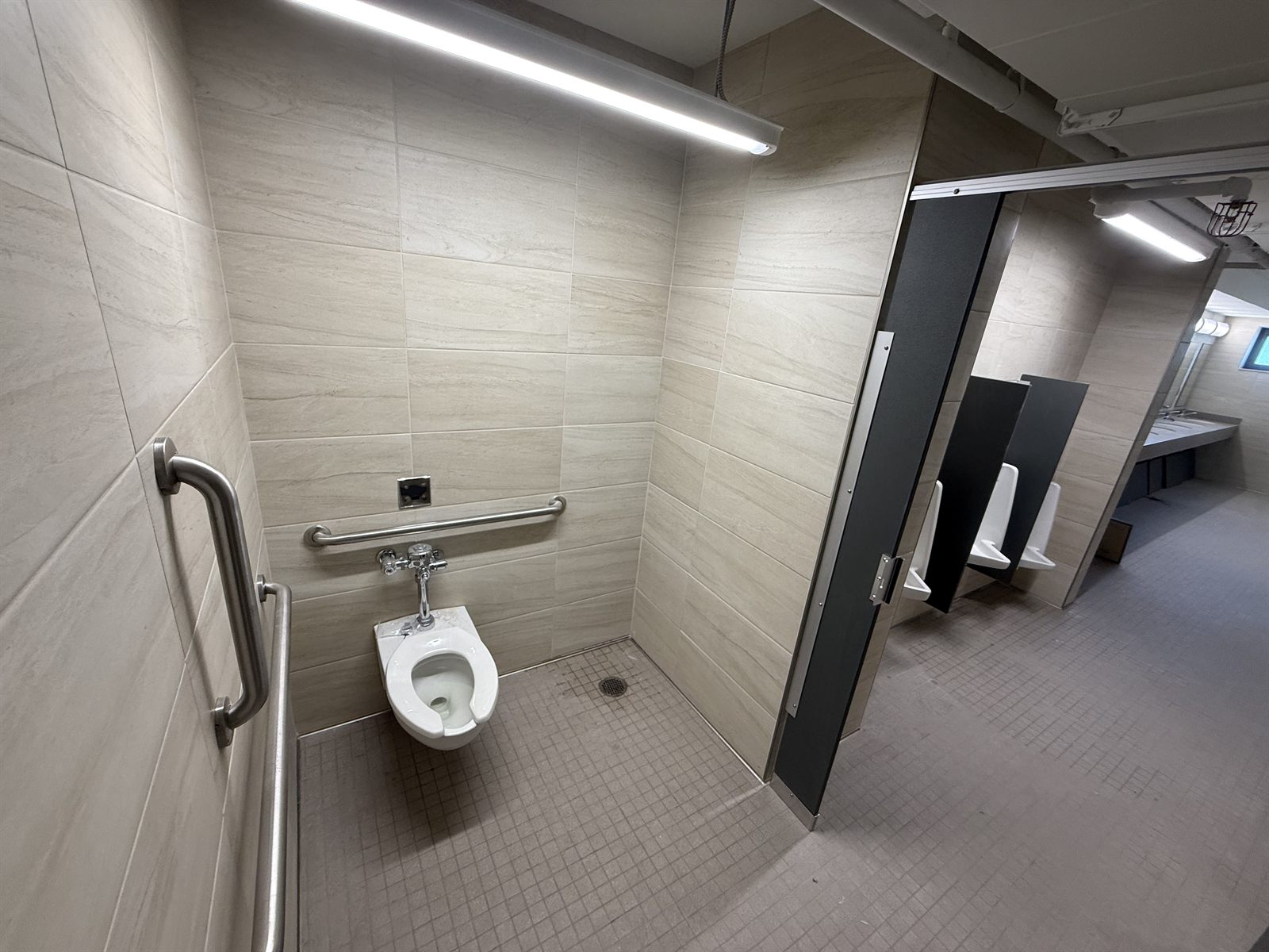 Public restroom with beige large format plank wall tile, small square mosaic floor and accessible stall
