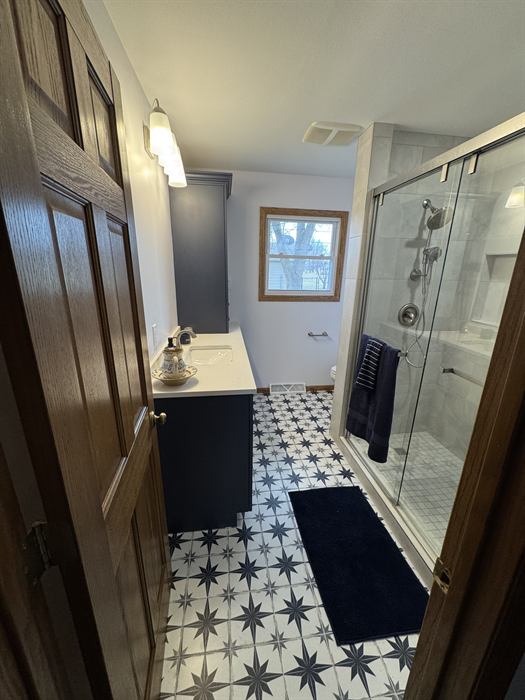 White and navy star pattern bathroom floor next to a glass walk-in shower in gray marble look tile