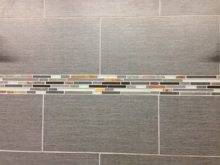 Close view of a linear glass and slate mosaic strip set between gray linen texture rectangular tiles