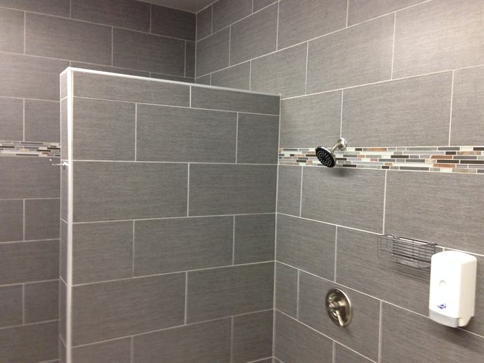 Shower stall with gray large rectangular wall tile, a tiled pony wall and glass mosaic accent band