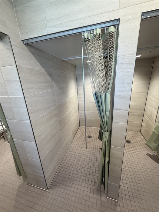 Row of shower stalls with light beige plank style wall tile and small square mosaic floor tile