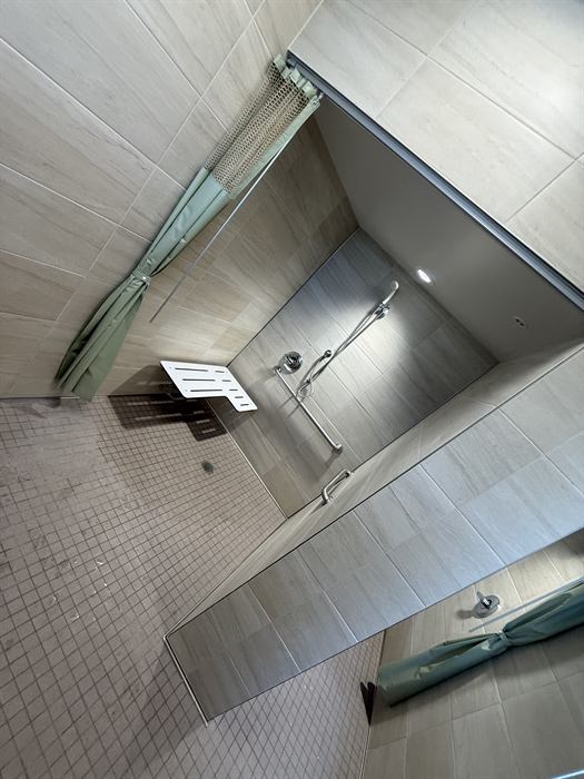 Accessible shower with beige plank wall tile, fold-down bench, handheld shower and square mosaic floor