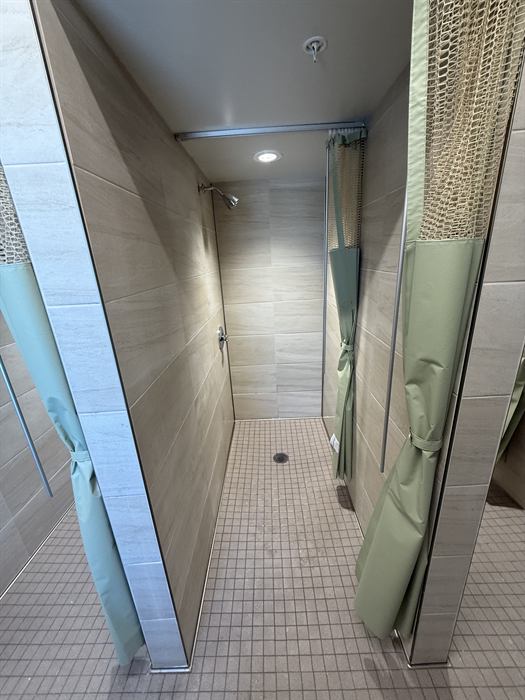 Locker room shower stalls with beige plank wall tile and small square mosaic floor
