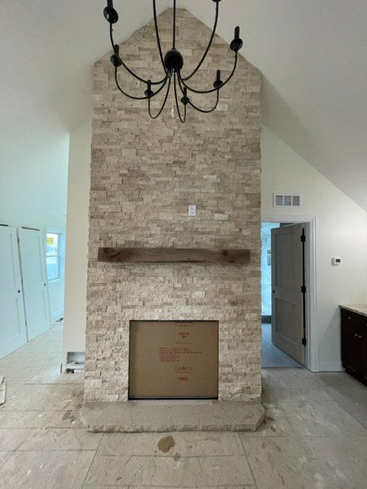 Floor to ceiling stacked stone fireplace in light beige stone with a wood mantel and a stone hearth, running up into a vaulted ceiling