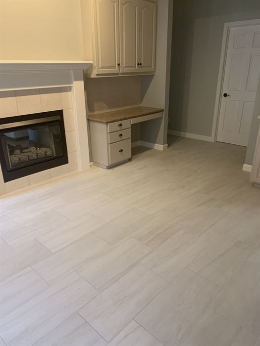 Light gray stone look rectangular floor tile in an offset layout beside a tiled gas fireplace