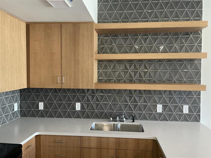 Gray dimensional geometric tile backsplash running full height behind floating wood shelves