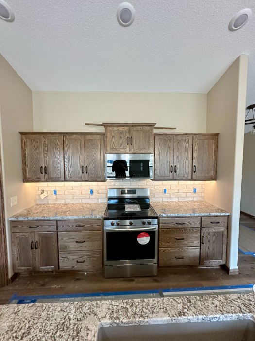 Cream handmade look brick tile backsplash behind a range, between oak cabinets with under cabinet lighting