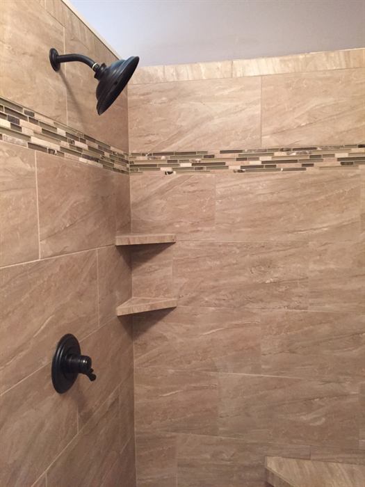 A travertine tiled shower with corner shelves and a glass mosaic accent band