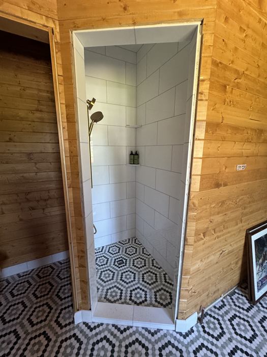 A tiled shower set into a cedar wall with a hexagon patterned floor