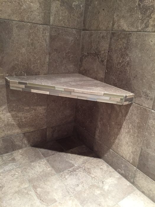 Corner shower bench edged with a linear glass mosaic strip, brown stone look walls and diagonal floor tile
