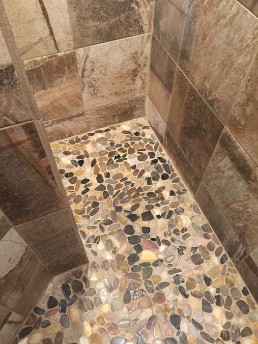Multicolor river pebble mosaic shower floor with large brown and gray stone look wall tile