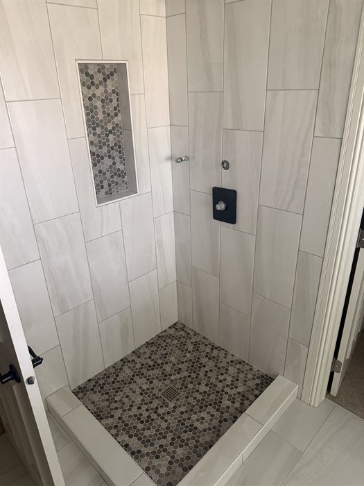 White marble look shower walls with a gray hexagon mosaic floor, matching niche and tiled curb