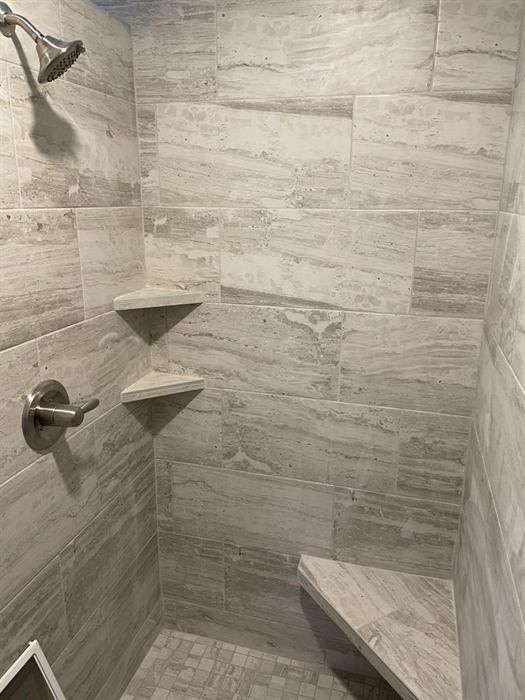 Gray vein cut stone look wall tile with corner shelves, corner bench and small mosaic floor